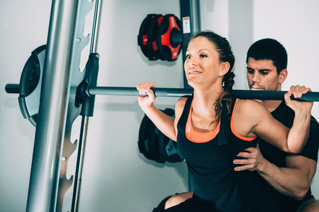 Personal training - Fitness trainer helping his client with weights in modern gymの写真素材