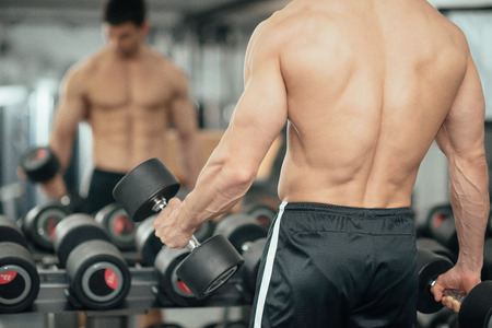 Workout with weights - Muscular young man working out with weights in gym, standing in front of mirrorの写真素材