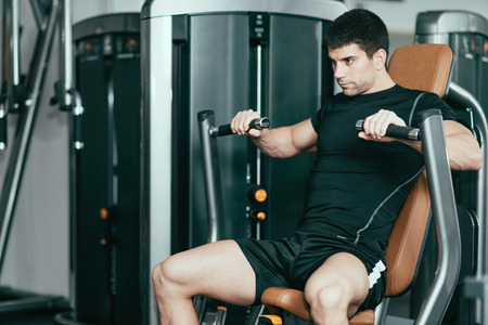 DSLR photo of male athlete training on new chest press exercising machine in modern gym. Model is...
