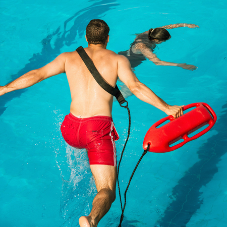 Lifeguard jumping into a swimming pool to rescue drowning victimの写真素材