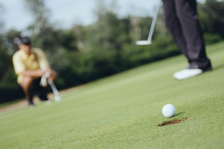 Detail from game of golf. Focus on ball, golfers in background, toned image