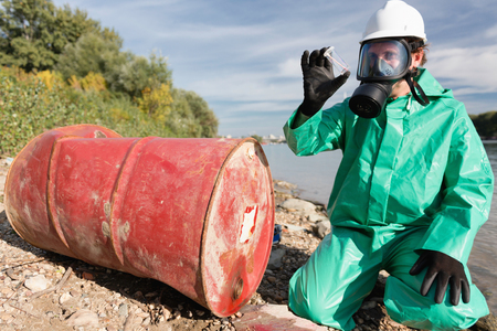 Pollution control official looking at sample of leaked chemicals collected by the riverの写真素材
