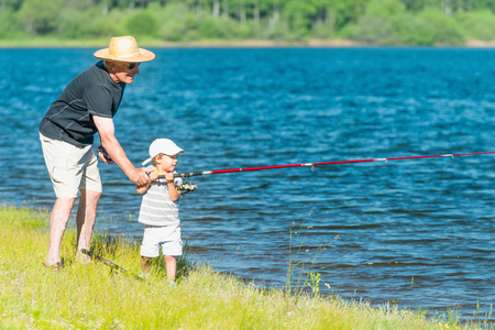 Grandfather and grandson enjoy fishing on the lakeの写真素材