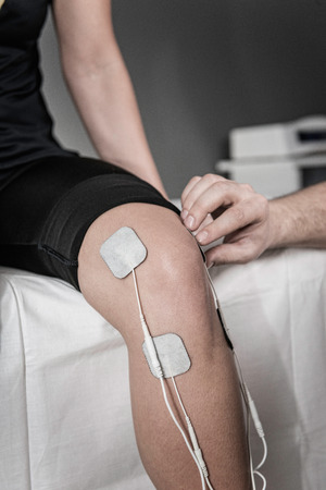 TENS treatment in physical therapy - therapist placing electrodes onto patient's kneeの写真素材