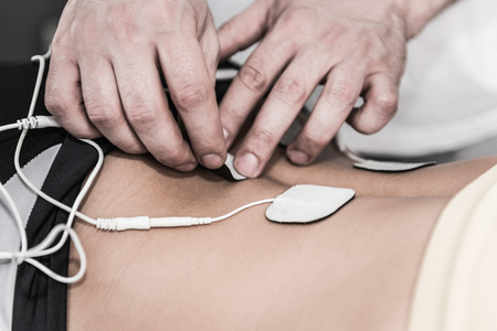 TENS treatment in physical therapy - therapist placing electrodes onto patient's lower backの写真素材