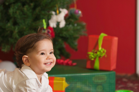 Smiling baby boy with Christmas tree and presents in the backgroundの写真素材