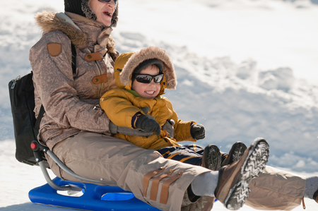 Mother and son sledding down hill, smiling, close-upの写真素材