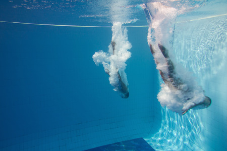 Two professional divers enter the water after a synchronized back flip dive. Underwater shot, convenient copy space on the left.の写真素材