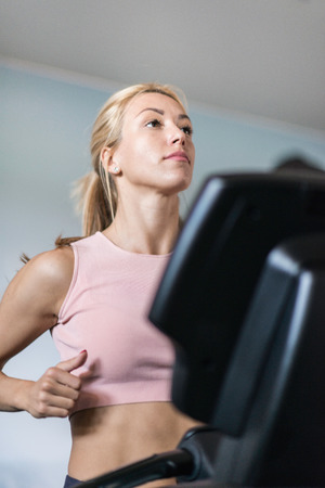 Attractive young woman running on treadmill. Selective focus, toned imageの写真素材