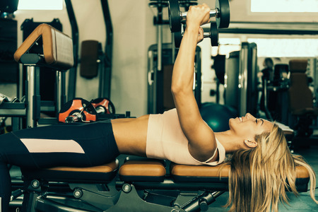 Beautiful young woman lying on the bench, working out with weights, smiling. Toned imageの写真素材