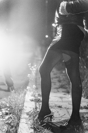 Street prostitution - roadside prostitute showing her legs. Photographed against headlights, black and white, fine grainの写真素材