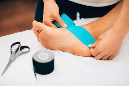 Kinesio taping in physical therapy - therapist placing kinesio tape to patient's footの写真素材