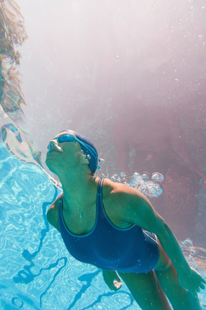 Underwater image of attractive female swimmer above the camera. Strange purple sunlight effect. Looking closely reveals body silhouette on the inner water surface.の写真素材