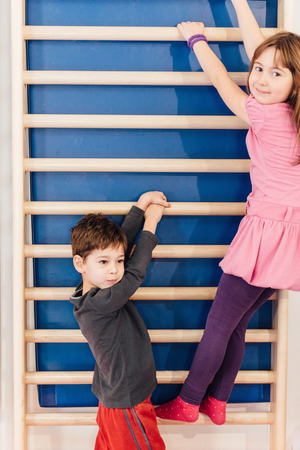 Little children hanging on wall bars in school gymnasium