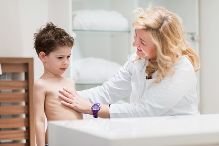 Physical therapist doing regular development medical exam with little boy, checking posture and functional status of spineの写真素材