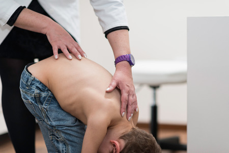 Physical therapist doing medical exam, checking functional status of spine of a little boyの写真素材
