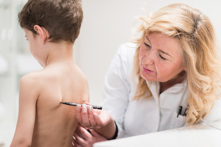 Physical therapist examining posture of a little boy, making marks on his back, checking angles of scapula bonesの写真素材