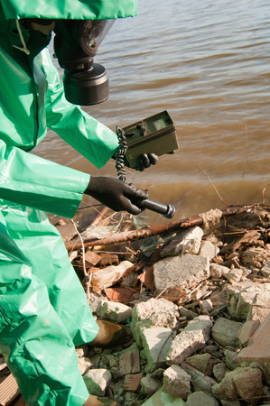 Technician in protective suit looking for traces of radiation on the shoreの写真素材