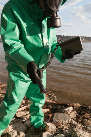Technician with geiger counter inspecting the shoreline. Extreme wide angleの写真素材