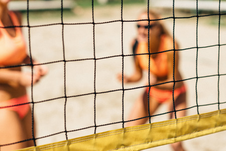 Beach volleyball net. Focus on net, cheerful girls behindの写真素材