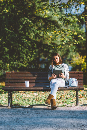 Teenage girl drinking coffe and using digital tablet in parkの写真素材