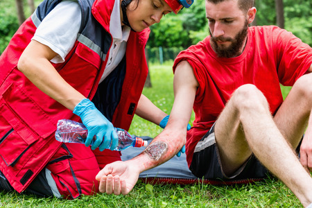 Medical worker treating burns on male's hand. First aid treatment outdoors. First aid practiceの素材 [FY31064272452]