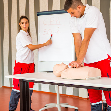 CPR class with instructors talking and demonstrating firt aid, compressions ans reanimation procedure. Cpr dummy on the table.の写真素材