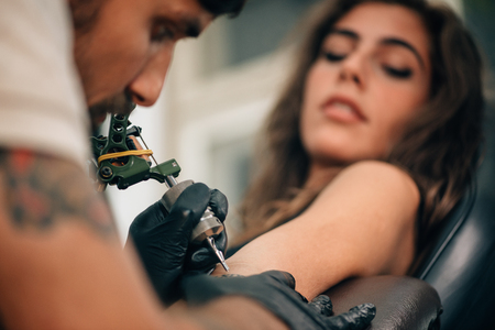 Tattoo artist creating a tattoo on a girl's arm. Focus on tattoo machineの写真素材