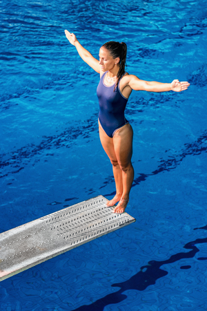 Female diver standing on the jumping board. Preparing to jump into the poolの写真素材