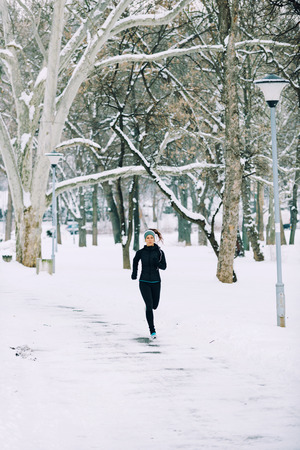 Female athlete jogging in park in winter with snow around the park. Listeninig music and exercisingの写真素材