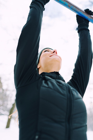 Female athlete exercising in park in winter with snow around the park. Listening music and...