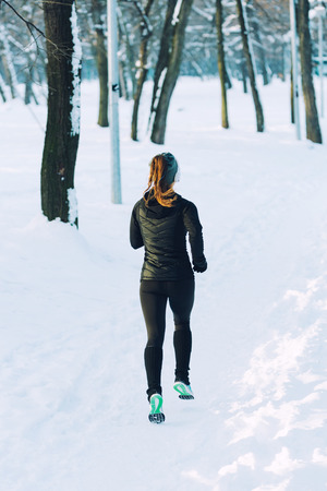 Female athlete jogging in park in winter with snow around the park. Listeninig music and exercisingの写真素材