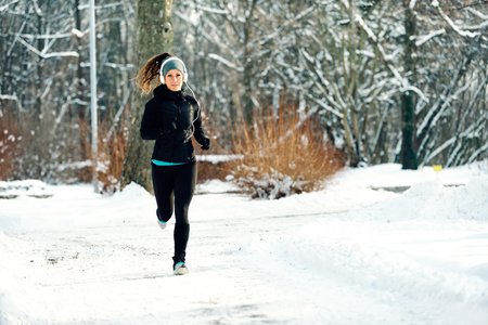 Female athlete jogging in park in winter with snow around the park. Listeninig music and exercisingの写真素材