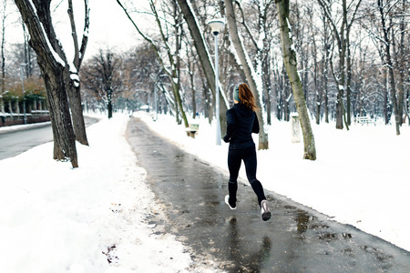 Female athlete jogging in park in winter with snow around the park