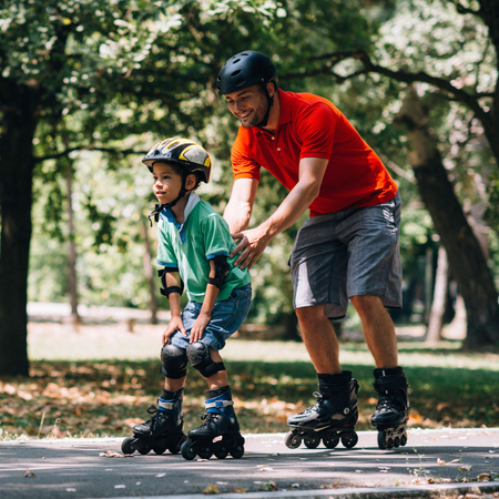 Father teching son roller skating in parkの写真素材