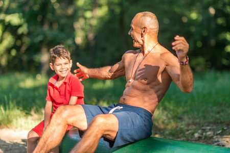 Grandfather and grandson doing sit-ups in parkの写真素材