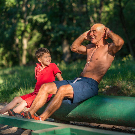 Grandfather and grandson doing sit-ups in parkの写真素材