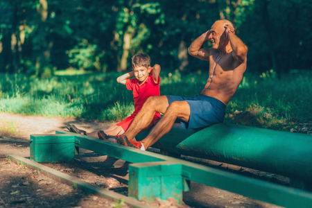 Grandfather and grandson doing sit-ups in parkの写真素材