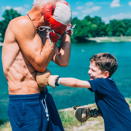 Little boy practicing boxing with grandfather by the lakeの写真素材