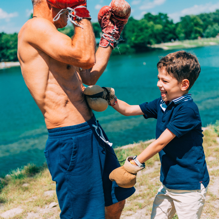 Little boy practicing boxing with grandfather by the lakeの写真素材