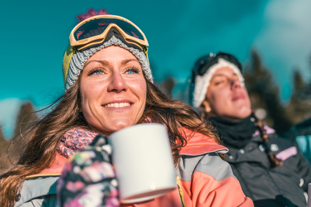 Friends enjoying the winter day on mountain. Drinking coffee or tea outdoorsの写真素材