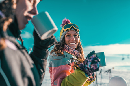 Friends enjoying the winter day on mountain. Drinking coffee or tea outdoors