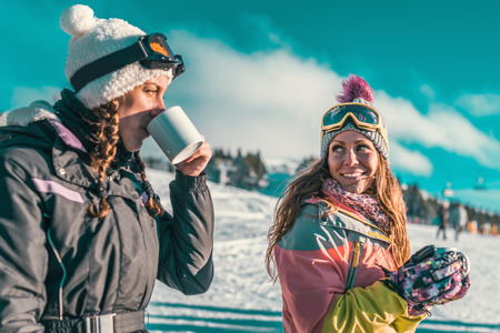 Friends enjoying the winter day on mountain. Drinking coffee or tea outdoorsの写真素材
