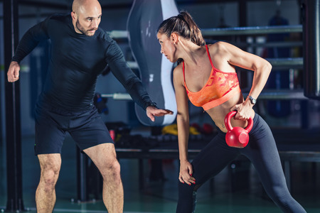 Personal trainer exercising with kettlebell with woman in the gymの写真素材