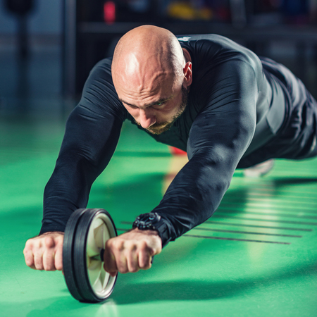 Man exercising abs on roller in the gymの写真素材