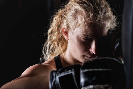 Young sporty female hitting the boxing bag, wearing black boxing glovesの写真素材