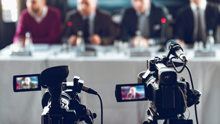 Two cameras recording presentation at press conference, blurred speakers wearing suit background, live streaming conceptの写真素材