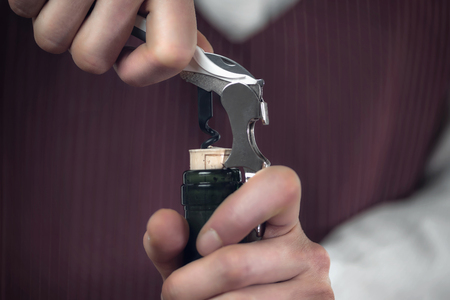 Female sommelier opening wine bottle with corkscrew, close up