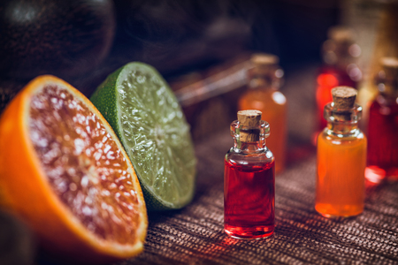 Bottles filled with red and orange essential oils. Fresh citrus fruit, orange and lime cut in half. Aromatherapy relax conceptの写真素材