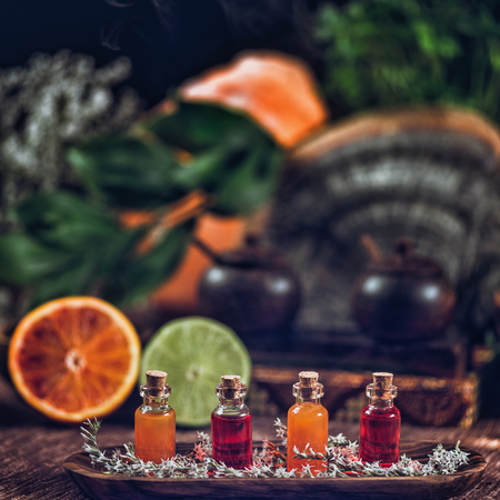 Bottles filled with red and orange essential oils on wooden board. Fresh citrus fruit, orange and lime cut in half. Aromatherapy relax conceptの写真素材